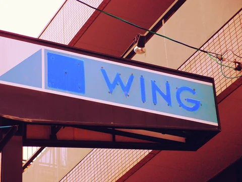 Blue WING lettering marks a projecting white sign beneath crossing wires and a hanging bulb.