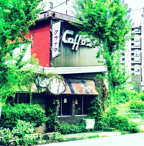 Dense vines surround a small cafe building with a large Coffee sign and weathered striped awning.
