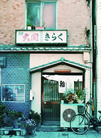 A bicycle leans beside an air conditioner outside a narrow entrance framed by green tiles and plants.