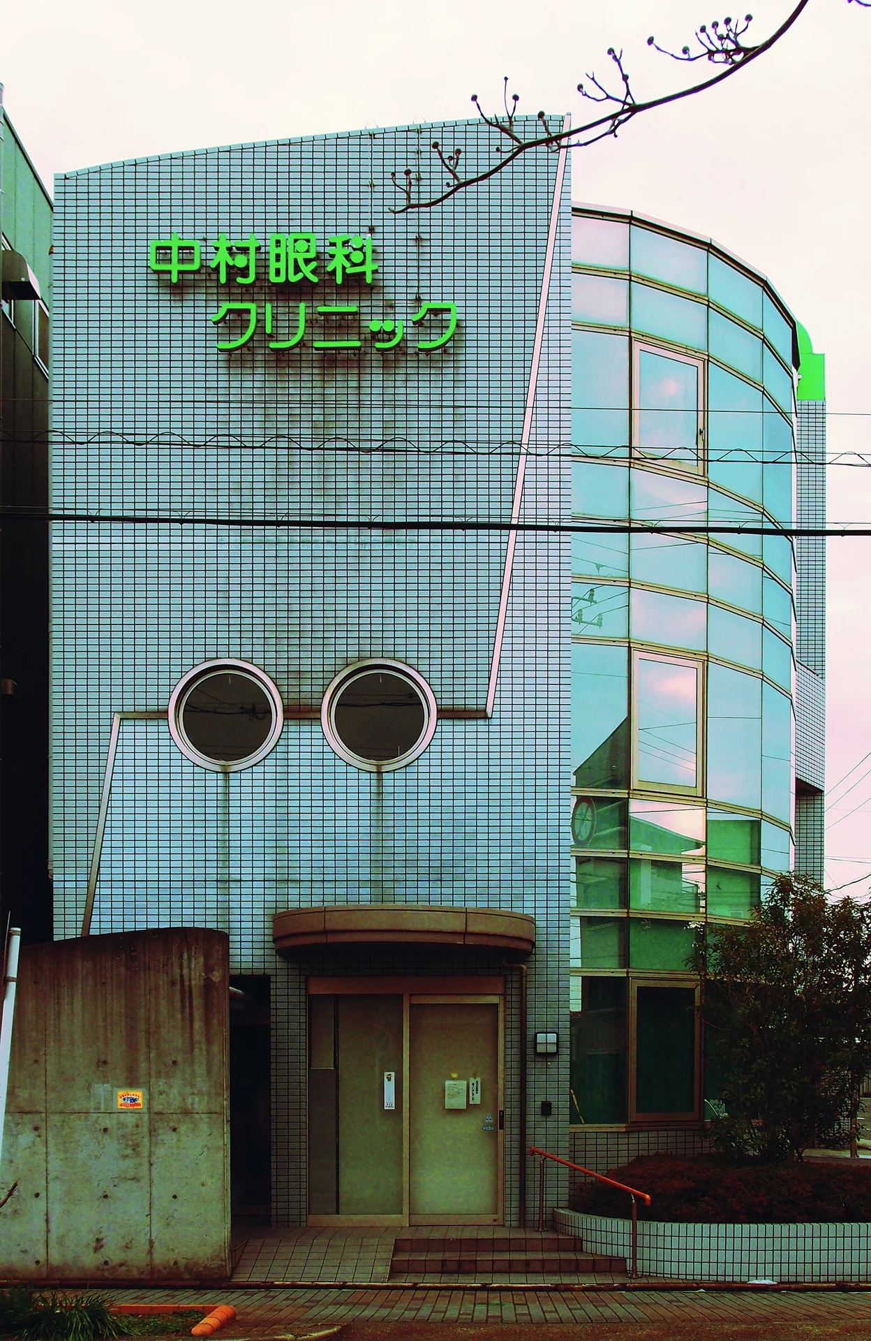 A pale blue tiled building has round windows and a curved glass-fronted corner.