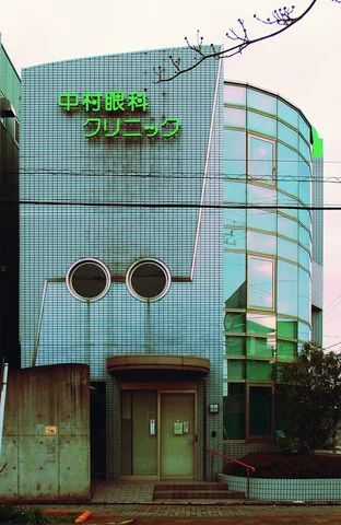 A pale blue tiled building has round windows and a curved glass-fronted corner.