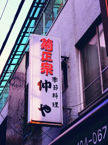A white vertical restaurant sign with red and black characters hangs against purple-toned siding.
