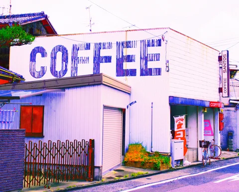 Huge blue COFFEE letters cover a pale corner building beside closed shutters and a narrow entrance.