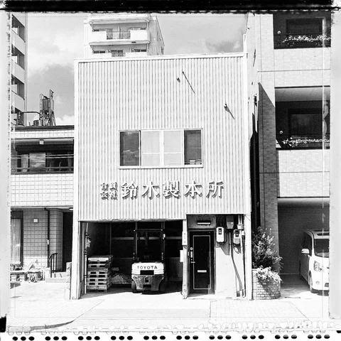 A small forklift sits in an open workshop below raised Japanese lettering on corrugated siding in black and white.