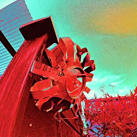 A red decorative wheel is mounted on a wooden support beneath turquoise sky.