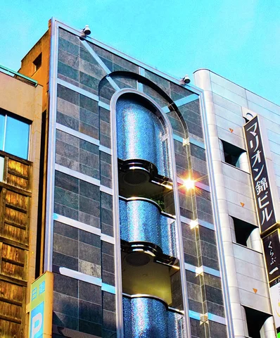 Three curved blue balconies fill a tall arched recess in a gray building beneath turquoise sky.