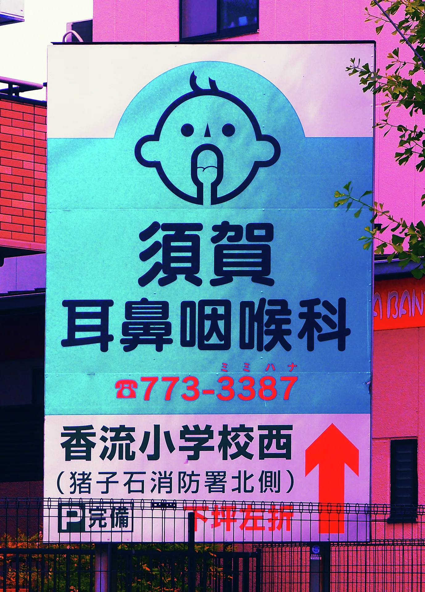 A cartoon face tops a turquoise Japanese clinic sign with a large red upward arrow.