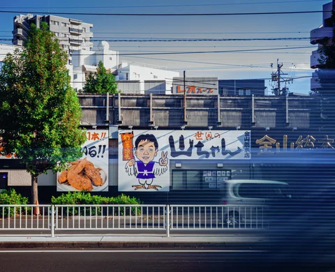 Illustrated restaurant signs span a roadside building behind white railings and a blurred passing vehicle.