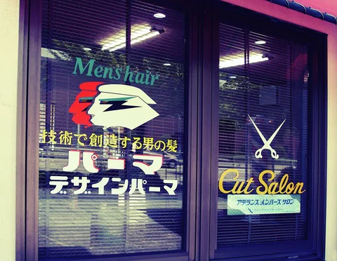 A stylized profile and scissors decorate glass salon doors with colorful lettering.