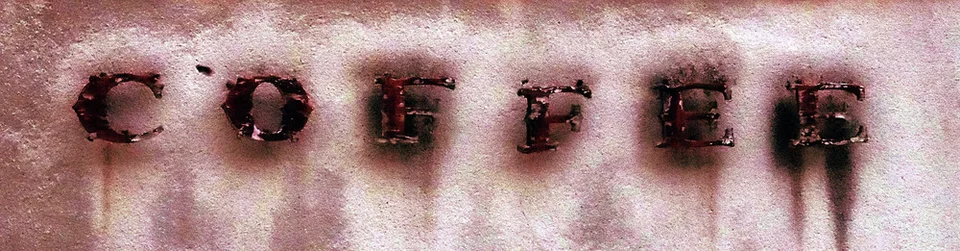 Dark raised COFFEE letters leave long rust stains down a pale textured wall.