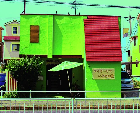 A bright green building with a red shutter has a small umbrella outside its entrance.