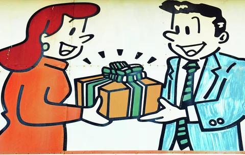 A cartoon woman and smiling suited man hold a yellow gift box tied with a green ribbon.