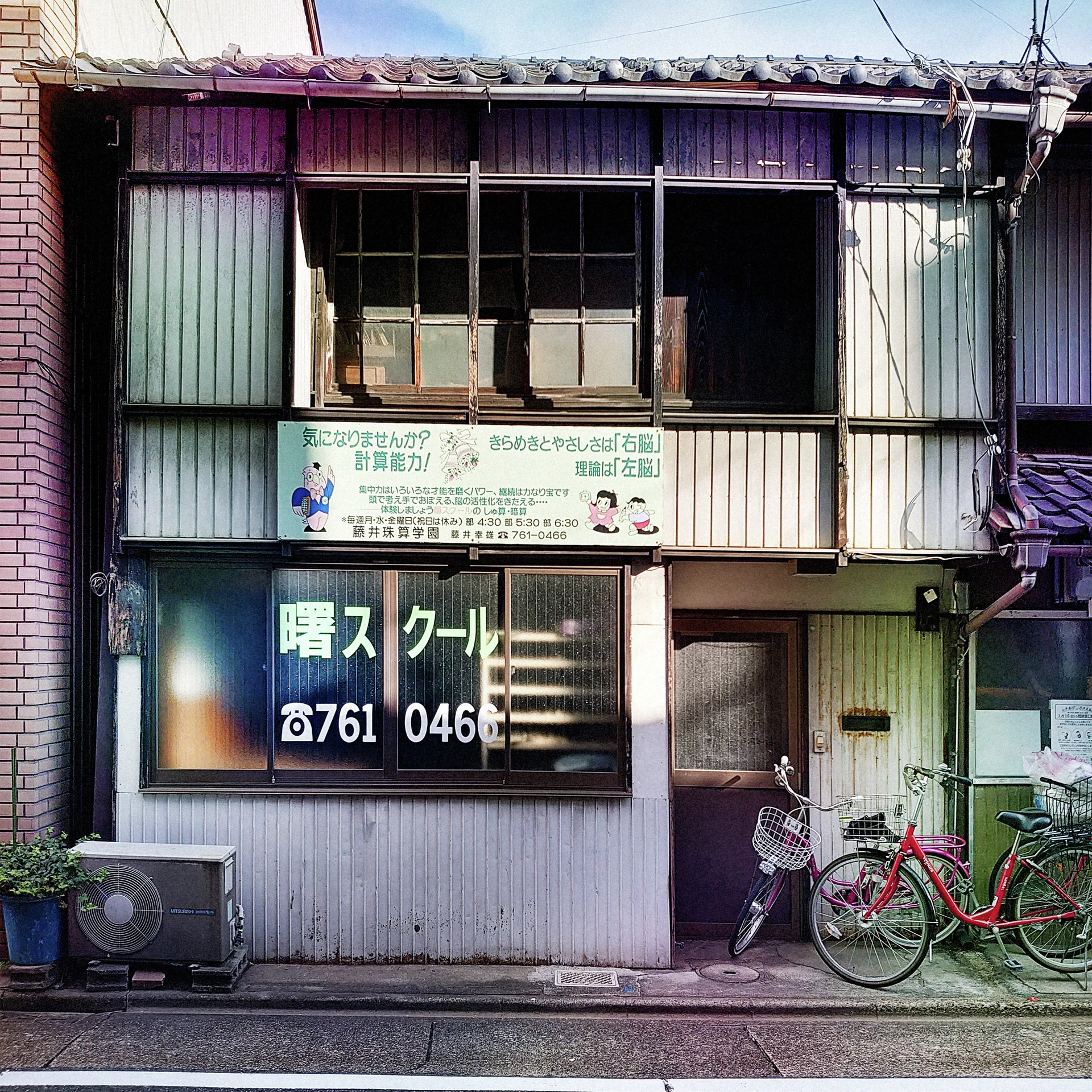 Two bicycles stand outside a weathered corrugated building with dark upstairs windows and a large frosted shop window.