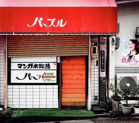 White Japanese lettering marks a red awning above a partly closed shutter and orange doorway.