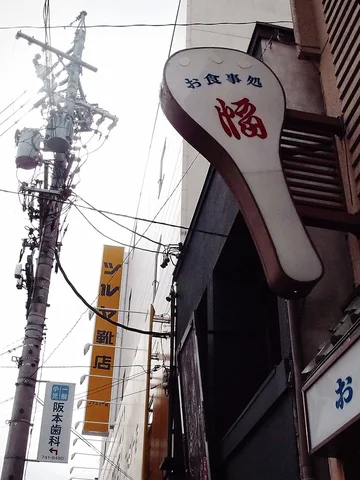 A pale paddle-shaped Japanese sign projects beside a utility pole crowded with cables and transformers.
