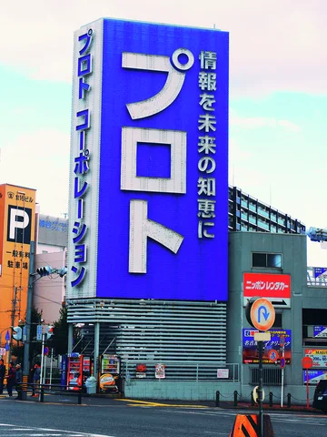 A tall blue sign with oversized white characters rises beside a broad urban roadway.