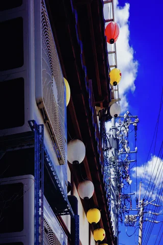 Red, white, and yellow lanterns line a building beside utility wires and blue sky.