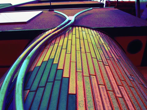 Curving turquoise pipes climb a rounded facade covered in narrow multicolored rectangular tiles.