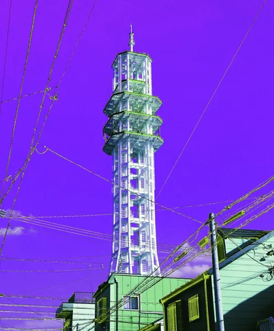 A metal lattice tower with circular platforms rises above low buildings and wires beneath a purple sky.