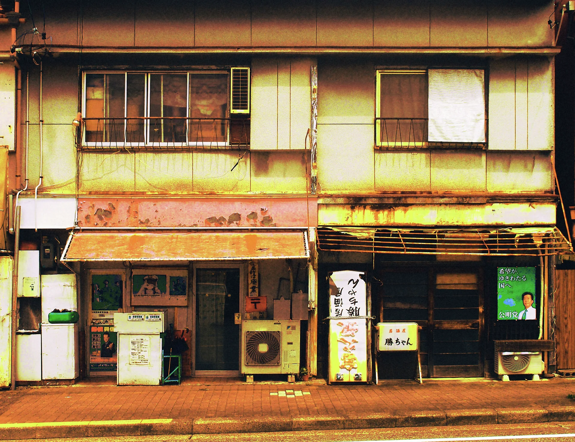 Two narrow ground-floor storefronts sit beneath stained upper walls and windows, with awnings, signs, and outdoor air conditioners.