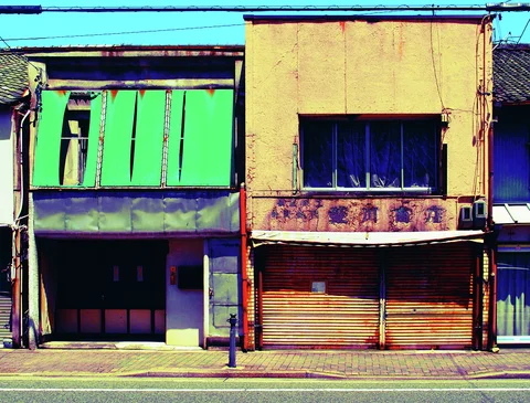 Green upper panels adjoin a yellow weathered storefront with dark windows and closed orange shutters.