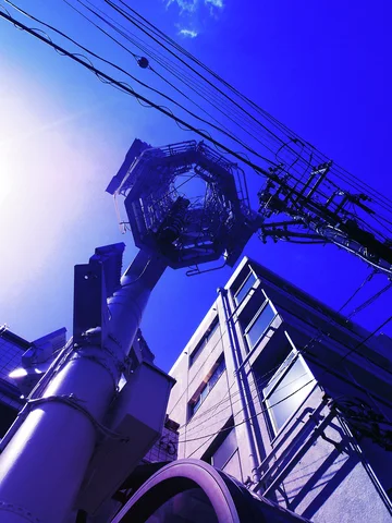 An ornate streetlight head silhouettes beside utility wires and a building beneath blue sky.