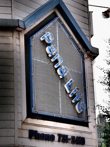 Angled pale letters descend across a dark mesh sign framed by a pointed blue border.