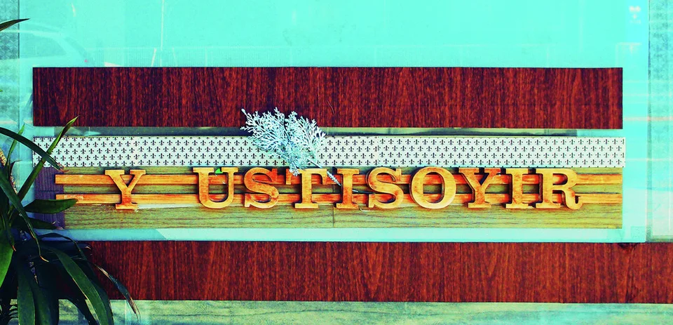 Raised gold lettering spans a layered reddish sign panel beneath a decorative patterned strip.