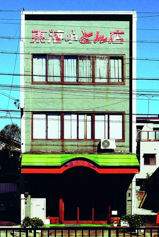 A narrow green-paneled building has red upper lettering and a curved red-trimmed storefront awning.
