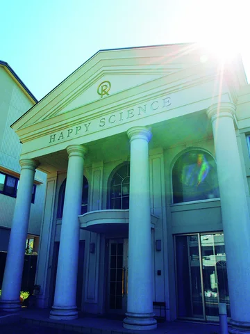 Tall pale columns support a triangular pediment above arched windows with bright sunlight flaring at the roof.