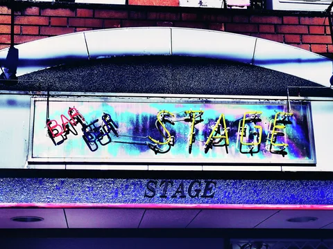 Multicolored neon Bar and Stage lettering decorates a reflective panel beneath a broad white arch.