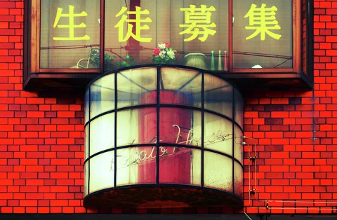 A curved translucent canopy projects from a red brick facade beneath windows with large yellow Japanese characters.