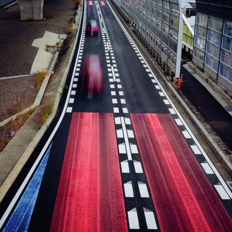 Blurred red vehicle trails extend along a narrow road marked with red rectangles and dashed white lines.