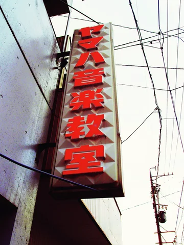 Raised red characters run down a pale vertical sign beside tangled overhead wires.
