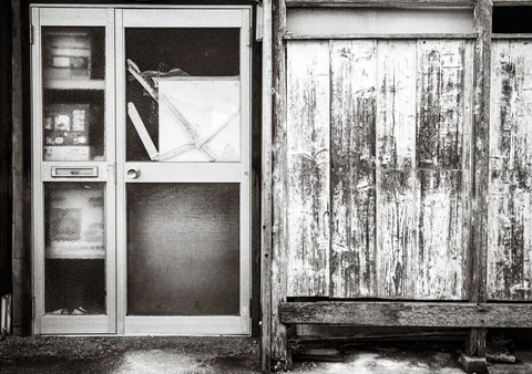 A frosted glass door stands beside heavily weathered wooden boards in a black and white facade.