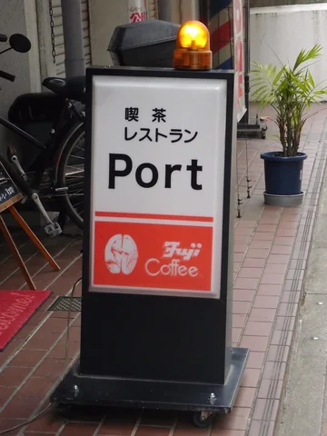 A black freestanding Port cafe sign has a red coffee panel and glowing amber beacon.