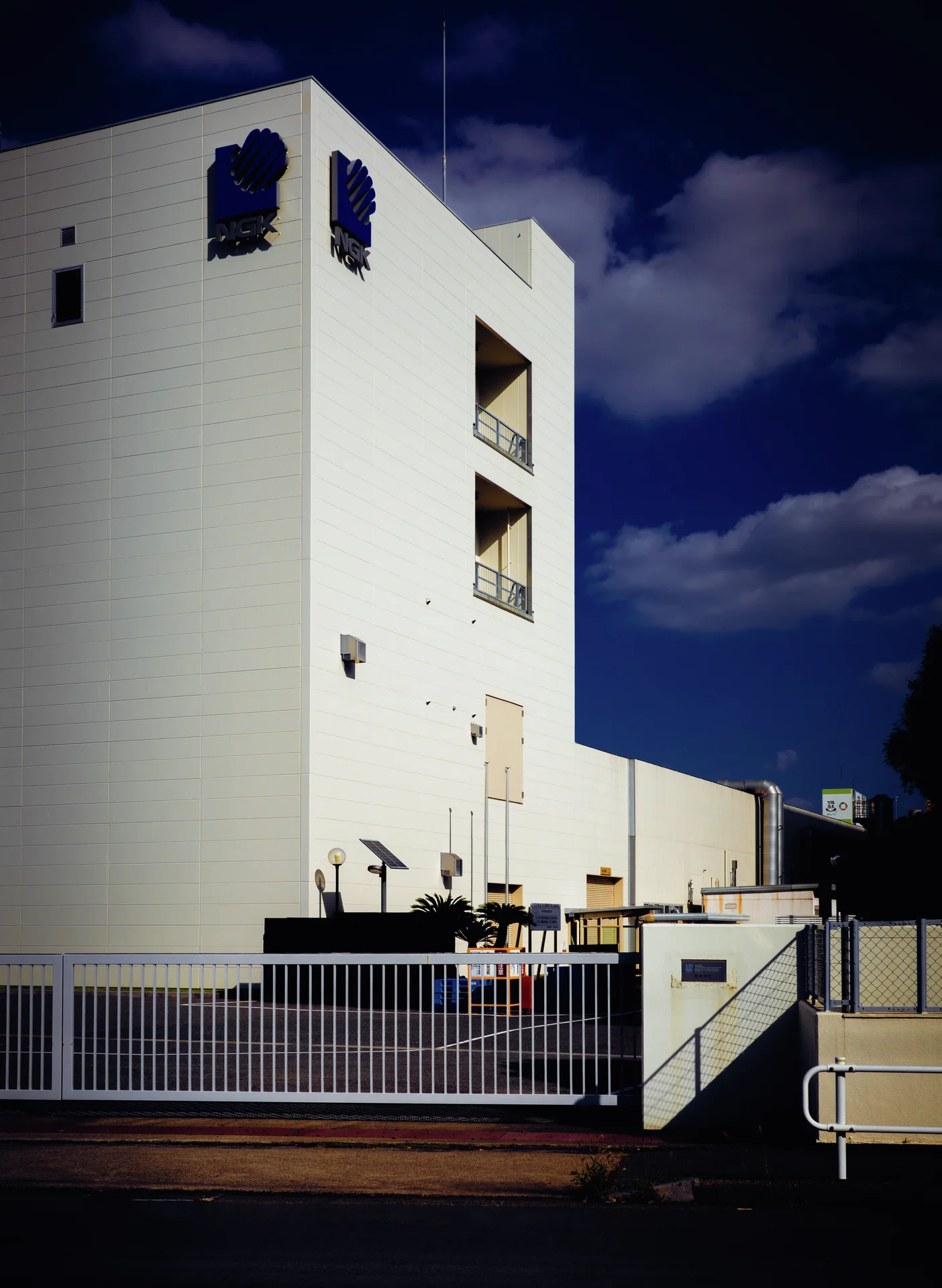 A tall pale building with small square windows rises above a metal railing beneath deep blue sky.