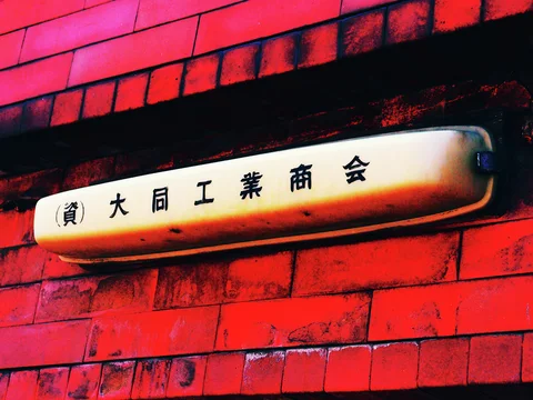 A narrow cream sign with black Japanese lettering projects from a vivid red brick wall.