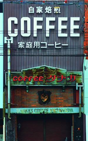 Large white COFFEE lettering tops a narrow dark storefront above red lettering and a closed shutter.