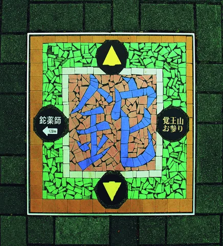 A colorful mosaic panel with blue Japanese characters and yellow arrows is set into a gray block wall.