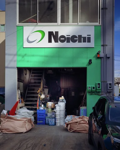 Buckets and bundled materials fill the entrance of a green-fronted workshop beneath a white sign.