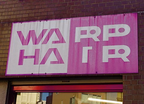 A weathered pink and white Warp Hair sign spans a brick storefront above a narrow entrance.
