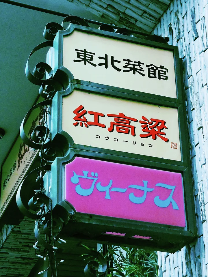 Three stacked sign panels with black, red, and blue lettering hang beside round projecting lamps.