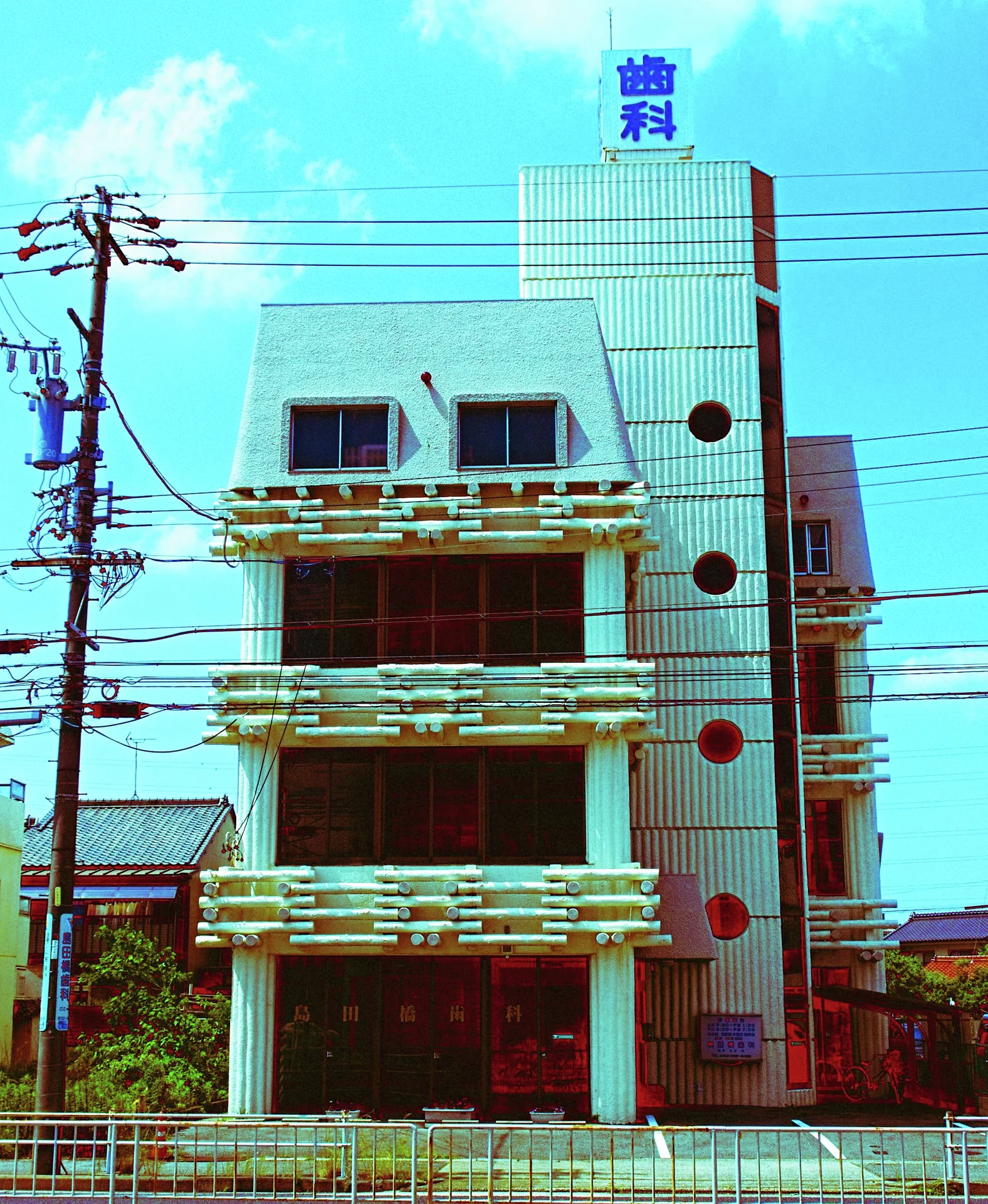 A narrow pale building combines decorative balcony rails and circular side windows behind overhead wires.