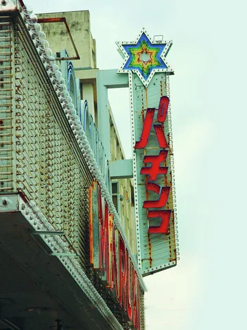 A star-shaped ornament crowns a tall projecting sign with large red Japanese letters beside a textured facade.