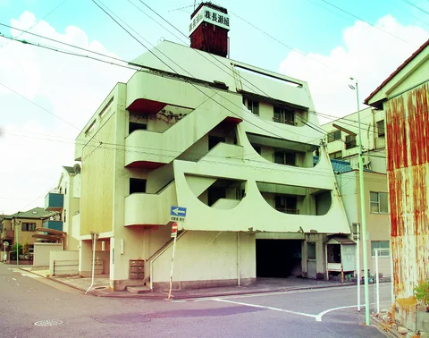 Curved pale exterior stair walls zigzag up a corner building beneath dense overhead wires.