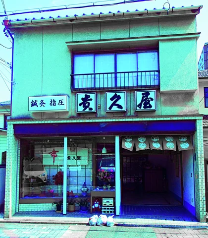 Black Japanese characters fill white sign panels beneath an upper window on a green-toned storefront.