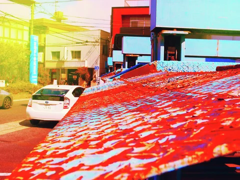 Peeling red and blue paint covers a low roof beside parked cars and brightly colored buildings.
