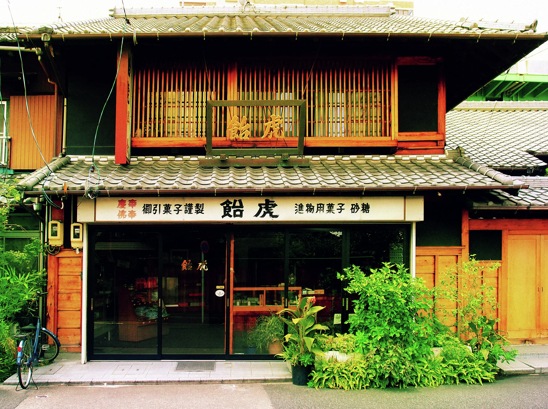 Plants fill a wooden shop frontage beneath tiled roofs and a long row of upper lattice windows.