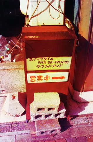 A small red standing sign with Japanese lettering rests on concrete blocks beside a dark entrance.